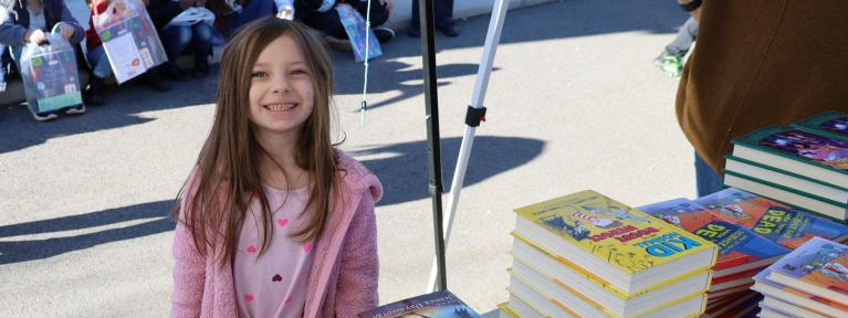 Girl smiling in front of a stack of books