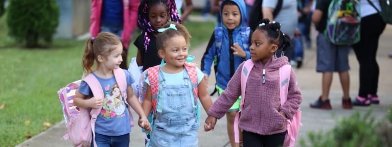 Three girls with backpacks holding hands outside