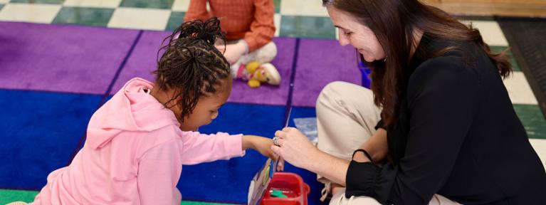 Teacher and student sitting on colorful rug doing an activity