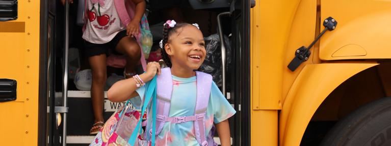 Smiling girl  with backpack exiting school bus